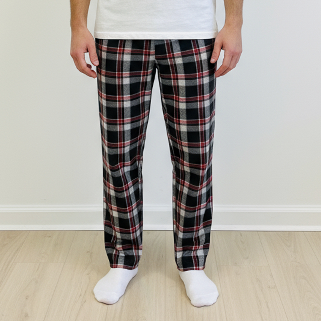 Man wearing a white t-shirt and plaid pajama pants standing against a plain white wall.